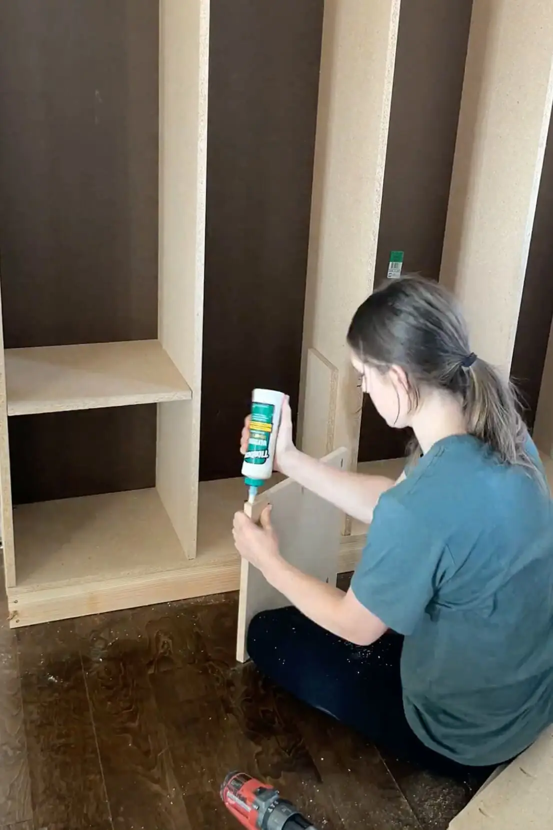 DIYer applying wood glue to a divider panel while assembling custom-built mudroom lockers.